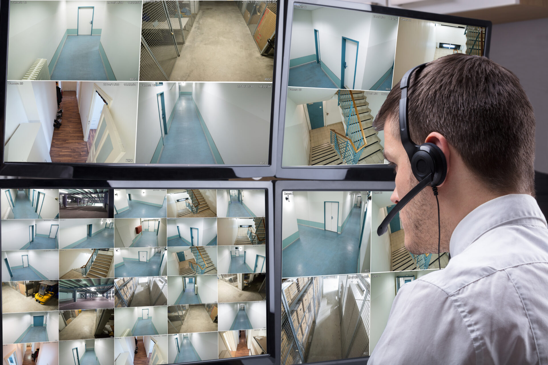 Rear View Of A Male Operator Wearing Headphone Looking At Multiple Camera Footage On Computer